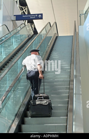 Airline pilot at airport going up escalator with luggage Stock Photo