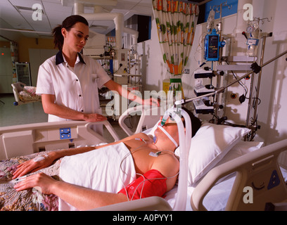 Hospital nurse tending to male patient in intensive care unit. Stock Photo