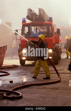 Fireman spraying water from a hose mounted on a the ladder bucket of a ...
