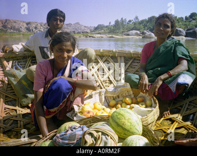 Pair of ambulant woman & man fruit sellers crossing the Tungabadhra river on straw raft Hampi Karnataka India South Asia Stock Photo