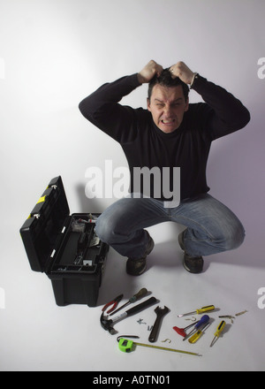 Man in casual clothes looks frustrated at the number of tools in his toolbox or angered at the complexity of a project in hand Stock Photo