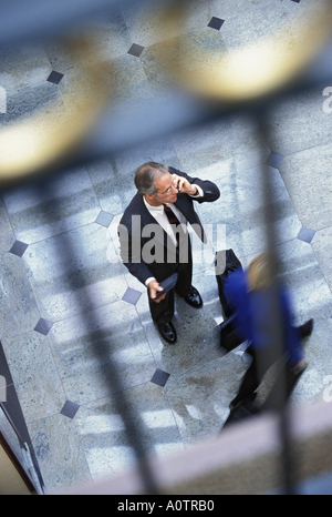 Overhead view of a Caucasian businessman gesturing and talking on cell phone in lobby Stock Photo