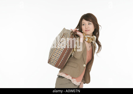Side profile of a young woman carrying a suitcase over her shoulder Stock Photo