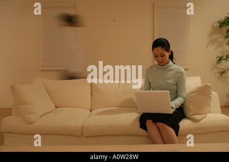 Young woman sitting on a couch and using a laptop Stock Photo