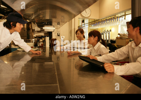 Waiters standing at a kitchen counter and talking to a chef Stock Photo