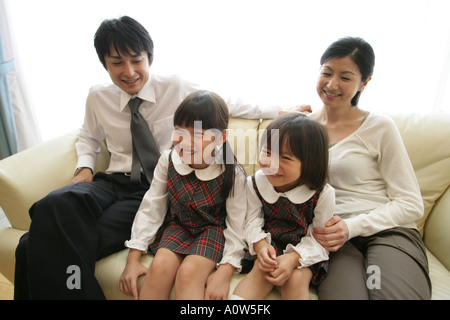 Mid Adult Couple and their daughters sitting on a Sofa and smiling Stock Photo
