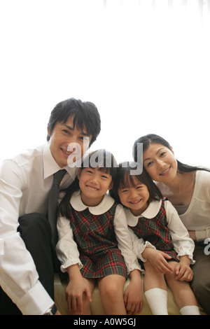 Portrait of a Mid Adult Couple and their daughters sitting on a Sofa and smiling Stock Photo