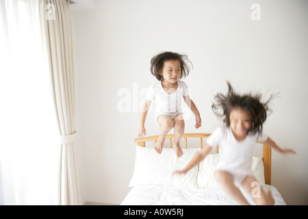 Girl and her sister jumping on the bed Stock Photo