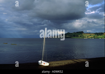 Storm clouds over a lone sail boat on a beach in Frutillar Chile Stock Photo