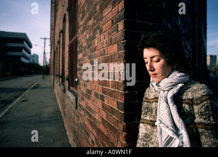 A pensive woman leans against a brick wall in an urban landscape Stock Photo
