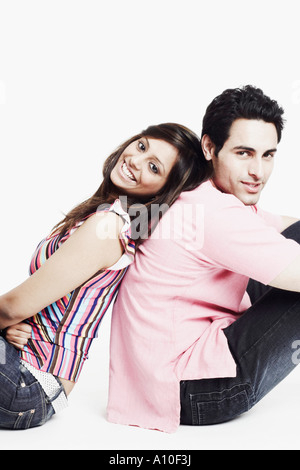 Portrait of a young couple sitting back to back on the floor and smiling Stock Photo