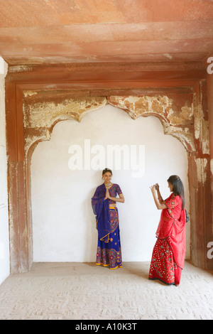 Young woman taking a photograph of her friend standing in a prayer position, Agra Fort, Agra, Uttar Pradesh, India Stock Photo