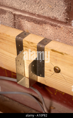 BUILDING AN EXTENSION A JOIST BOLTED TO A CONCRETE BLOCK WALL WITH A JOIST HANGER AND ELECTRICITY CABLES BENEATH Stock Photo