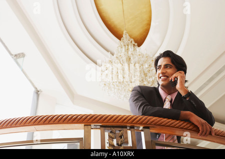 Low angle view of a businessman leaning over a railing and talking on a mobile phone Stock Photo