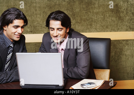 Two businessmen sitting in an office and using a laptop Stock Photo