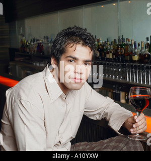 Portrait of a young man sitting at a bar counter and holding a glass of red wine Stock Photo
