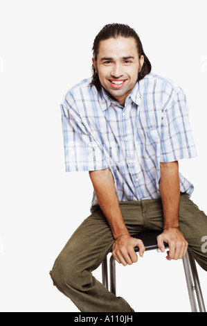 Portrait of a young man sitting on a stool and smiling Stock Photo