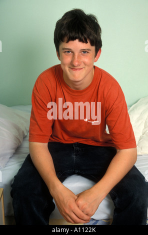 portrait dark haired teenage boy sitting on edge of bed Stock Photo