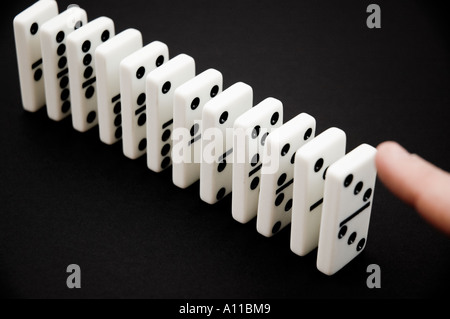 Dominos in a row on a black background being pushed over Stock Photo