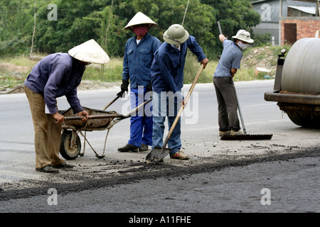 Workmen shovel in advance of the steamroller during  construction on the road from Saigon (HCMC) to the Mekong  Delta, Vietnam Stock Photo