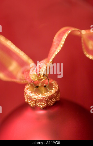 Red Christmas ornament with red and gold ribbon against a red background. Stock Photo