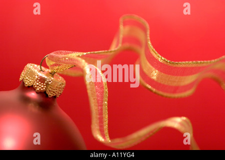 Red Christmas ornament with red and gold ribbon against a red background. Stock Photo