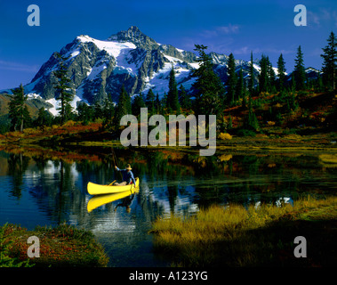 Canoe fishman netting a trout in Picture Lake under the towering snowcovered peak of Mount Shuksan in Northern Washington Stock Photo