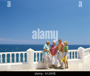 retired age couples leaning on balustrades and chatting with sea in background Stock Photo