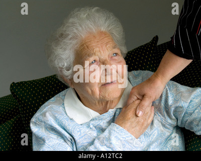 Contented independent elderly senior lady holds comforting hand of carer nurse in her room Horizontal Interior natural light Stock Photo