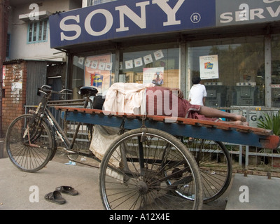 A laborer sleeps on a delivery vehicle near an electronics shop Stock Photo
