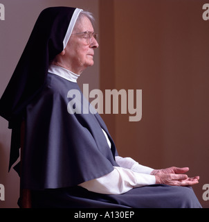 Nun sitting on chair praying. Stock Photo