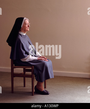 Nun sitting on chair praying. Stock Photo