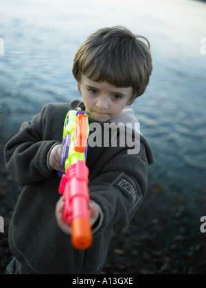 boy in the evening wearing fleece with large multicoroured water pistol looking worried Stock Photo