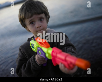 boy in the evening wearing fleece with large multicoroured water pistol looking worried Stock Photo