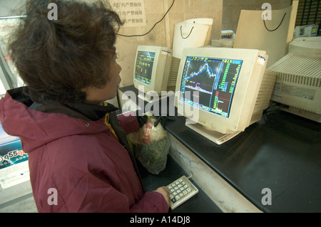 People trading in a Shanghai Stock market exchange branch open to the public, with screens displaying charts of share prices. Stock Photo