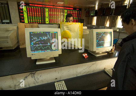 People trading in a Shanghai Stock market exchange branch open to the public, with screens displaying charts of share prices. Stock Photo