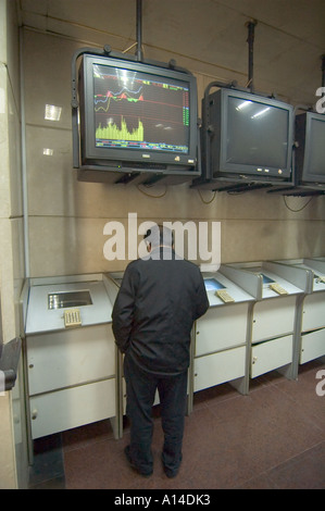 Man trading in a Shanghai Stock market exchange branch open to the public, under a screen displaying charts of share prices. Stock Photo