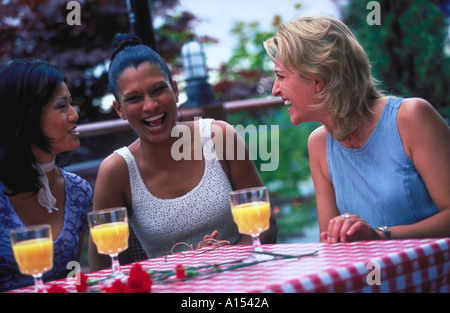 Three women sitting outside at a table with drinks laughing Stock Photo