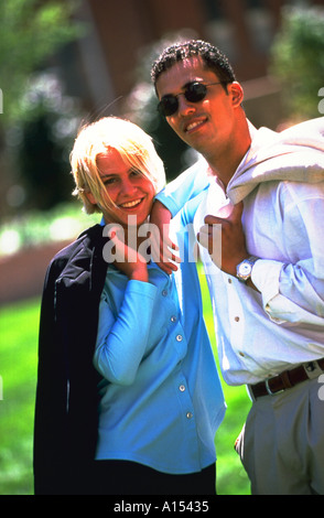 Portrait of a young couple standing together outside with their jackets thrown over their shoulders Stock Photo