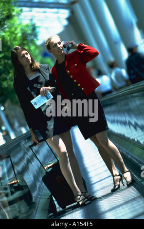 Two female executives standing on a moving sidewalk in an airport Stock Photo