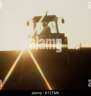 John Deere tractor ploughing a cereal stubble field on a winter evening with the sun behind Stock Photo