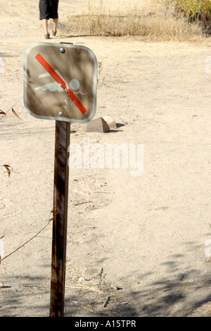A man walks behind a no swimming sign posted at a dried up oasis in the  desert. Stock Photo