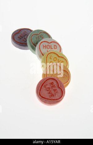 Vertical close up of a row of colourful loveheart sweets arranged in a line on a white background. Stock Photo