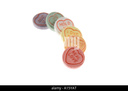 Horizontal close up of a row of colourful loveheart sweets arranged in a line on a white background. Stock Photo