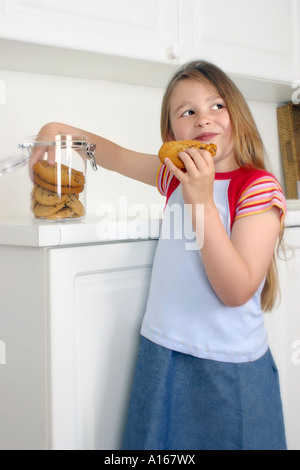 Girl eight years old taking cookies from jar Stock Photo