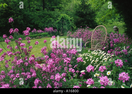 Gorgeous large private garden with purple Dames rocket, Phlox,  flowers, with rustic cedar arbor and bent willow chair and birdhouse Missouri USA Stock Photo