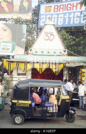 Indian street Hindu temple with OM written surrounded by modern hoardings and auto taxi at Borivali Bombay Mumbai India Stock Photo