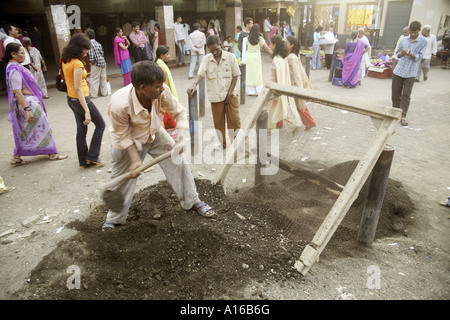 Road repair man sewing sand through wire mesh Bombay Mumbai India Stock Photo