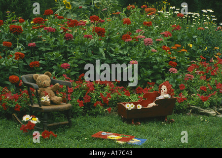 Childs antique toys including Raggedy Ann and stuffed Teddy Bear sitting in antique furniture outside in grass in colorful home garden Missouri USA Stock Photo