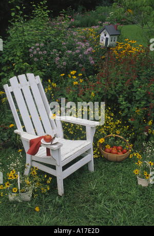 Private lunch in the garden: Fresh harvested tomato sits on a plate on a wooden chair with a basket of tomatoes and fancy painted birdbox, Midwest USA Stock Photo